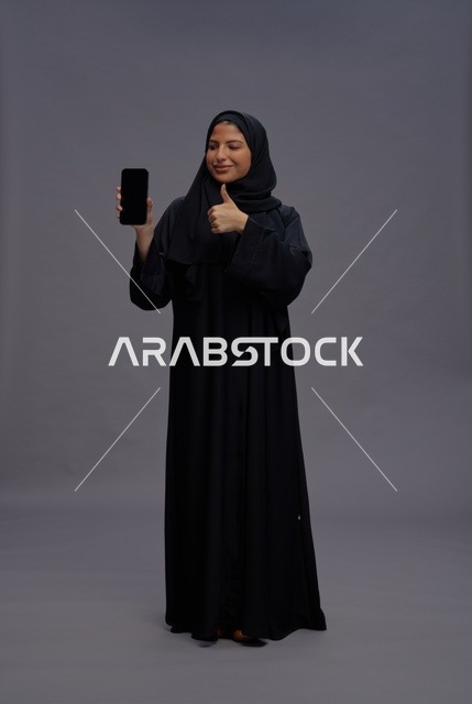 امرأة سعودية بالعباءة تمسك هاتف ذكي بشاشة فارغة