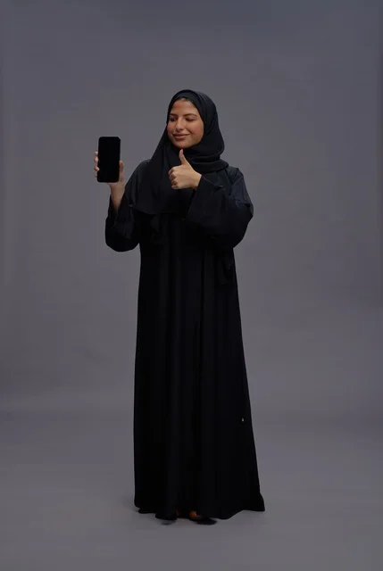 امرأة سعودية بالعباءة تمسك هاتف ذكي بشاشة فارغة