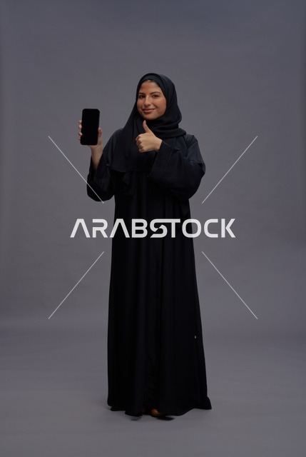 امرأة سعودية بالعباءة تمسك هاتف ذكي بشاشة فارغة