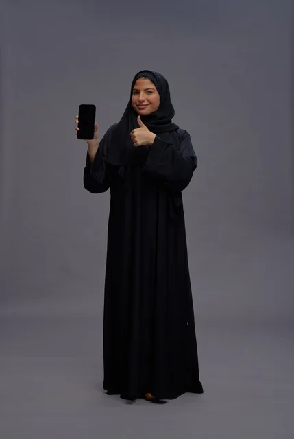 امرأة سعودية بالعباءة تمسك هاتف ذكي بشاشة فارغة