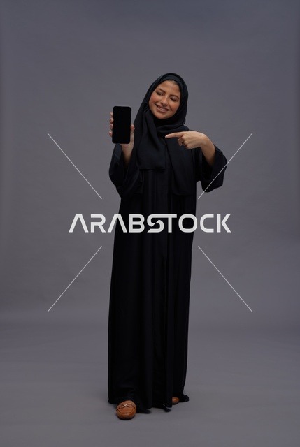 امرأة سعودية بعباءة تمسك هاتف ذكي بشاشة فارغة