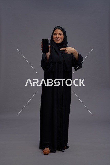 امرأة سعودية بالعباءة تحمل هاتف ذكي بشاشة فارغة