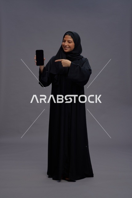 Saudi Woman in Abaya Pointing at Blank Smartphone Screen