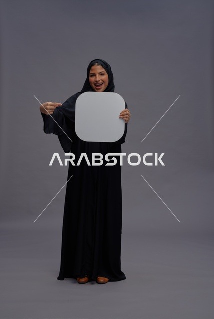 امرأة سعودية بالعباءة تحمل لوحة بيضاء فارغة للإعلان