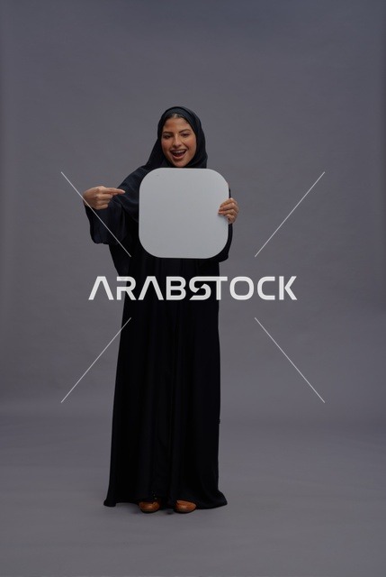 امرأة سعودية بالعباءة تشير إلى لوحة بيضاء فارغة