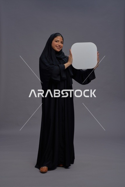 امرأة سعودية بالعباءة التقليدية تحمل لوحة بيضاء فارغة