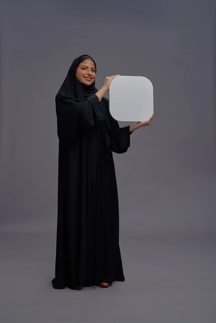 امرأة سعودية بالعباءة تمسك لوحة بيضاء فارغة