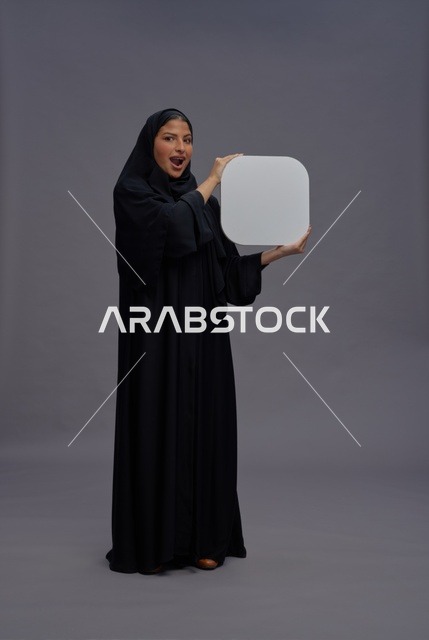 امرأة سعودية بالعباءة تحمل لوحة بيضاء بتعبير مندهش