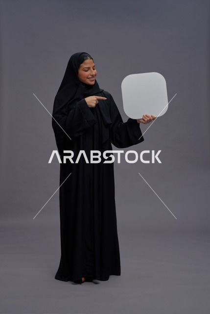 امرأة سعودية بالعباءة السوداء تحمل لوحة بيضاء فارغة