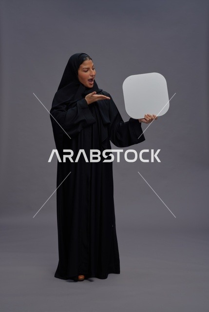 امرأة سعودية مندهشة بالعباءة تحمل لوحة إعلانية بيضاء
