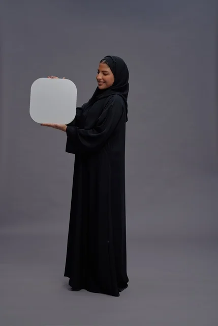 امرأة سعودية بالعباءة السوداء تحمل لوحة بيضاء فارغة
