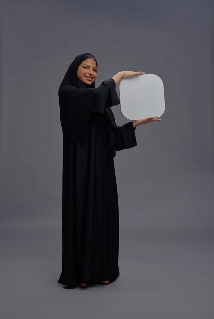امرأة عربية بالعباءة تحمل لوحة بيضاء فارغة في استوديو امرأة عربية بالعباءة تحمل لوحة بيضاء فارغة في استوديو