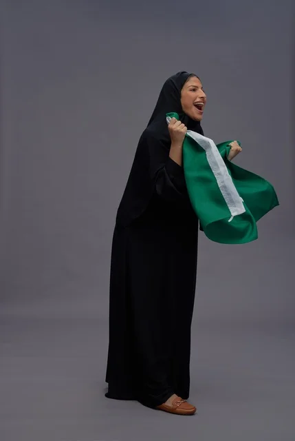 امرأة سعودية تحمل علم المملكة وتفخر بالاستوديو