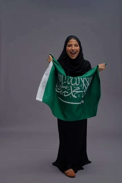 Saudi Woman Holding National Flag Against Grey Background