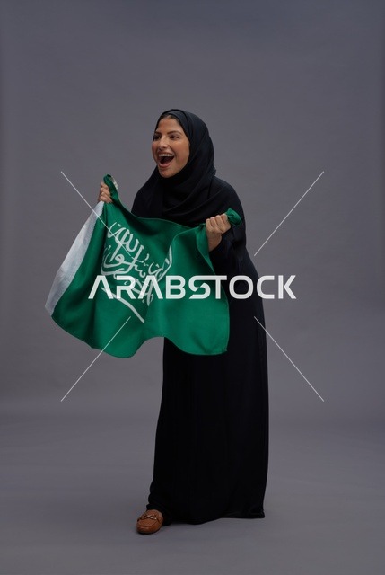 امرأة سعودية تحمل علم المملكة العربية السعودية بخلفية رمادية