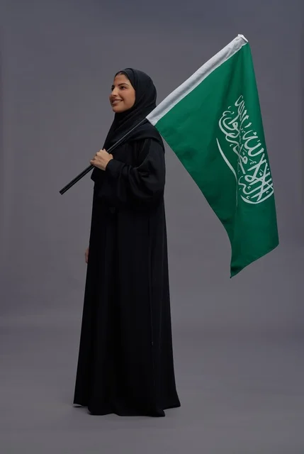 امرأة سعودية مع العلم الوطني في خلفية استوديو