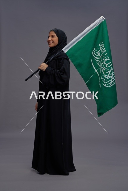 امرأة سعودية تحمل علم المملكة بخلفية رمادية