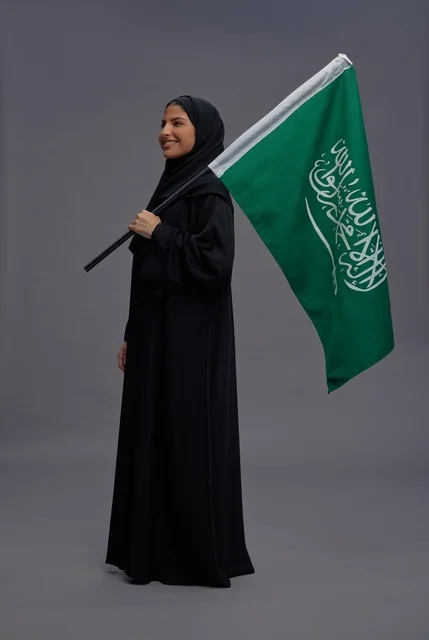 امرأة سعودية تحمل علم المملكة بخلفية رمادية