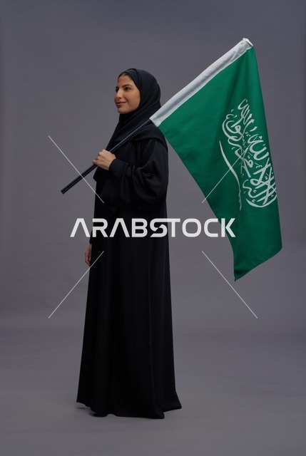 امرأة سعودية تمسك علم المملكة بخلفية رمادية