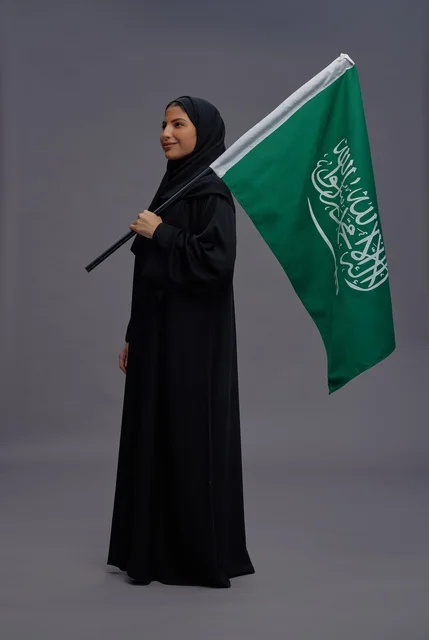 امرأة سعودية تمسك علم المملكة بخلفية رمادية