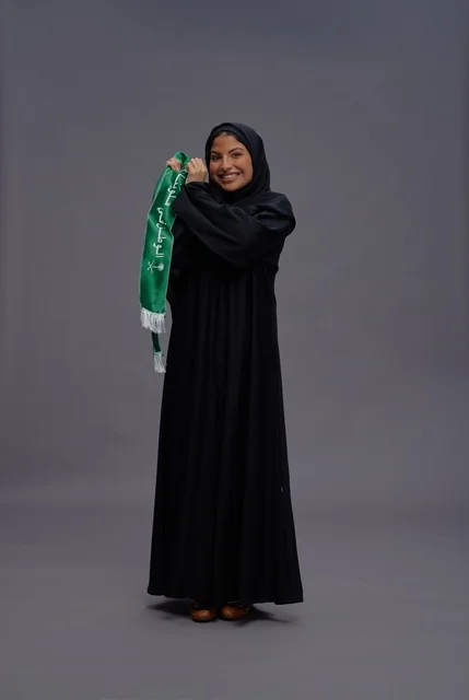 امرأة سعودية مبتسمة تمسك علم المملكة في الاستوديو