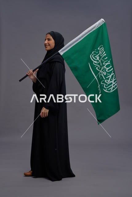 امرأة سعودية تحمل العلم الوطني بالعباءة السوداء