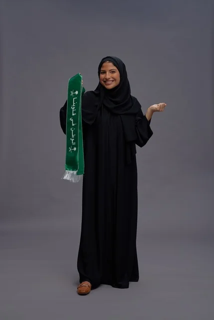 امرأة سعودية تحمل علم المملكة بالعباءة السوداء
