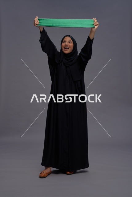 Saudi Woman Holding Saudi Flag Against Grey Background