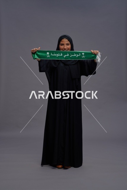 امرأة سعودية بالعباءة السوداء تمسك وشاحاً وطنياً أخضر