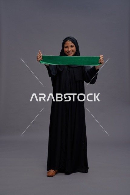 امرأة سعودية بالعباءة السوداء تمسك بعلم المملكة