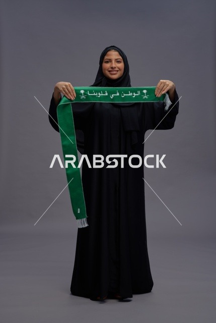 امرأة سعودية تمسك بوشاح وطني على خلفية رمادية