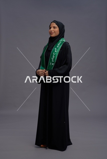 امرأة سعودية بالعباءة السوداء تمسك وشاح الوطن الأخضر
