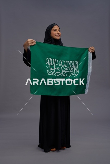 امرأة سعودية بالعباءة تمسك علم المملكة العربية السعودية