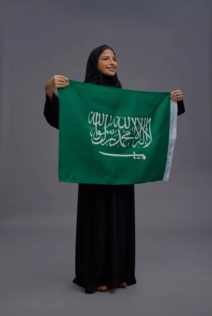 امرأة سعودية بالعباءة تمسك علم المملكة العربية السعودية