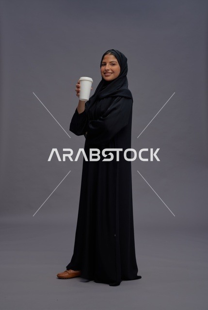 امرأة سعودية بعباءة سوداء تحمل كوب قهوة في الاستوديو