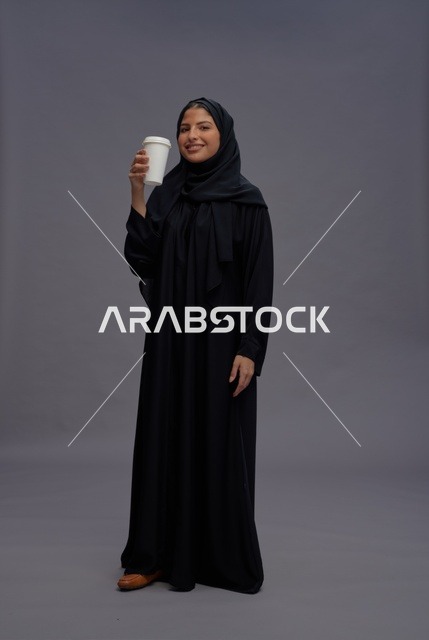 امرأة سعودية بالعباءة السوداء تحمل كوب قهوة في استوديو