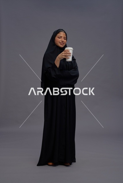 امرأة سعودية بالعباءة السوداء تحمل كوب قهوة