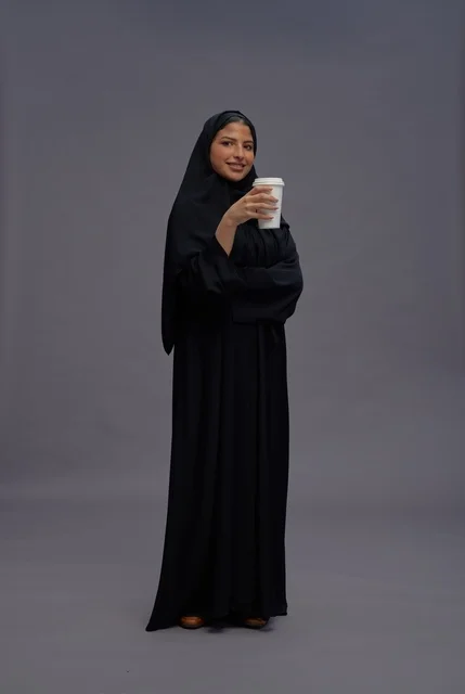 امرأة سعودية بعباءة سوداء تحمل كوب قهوة