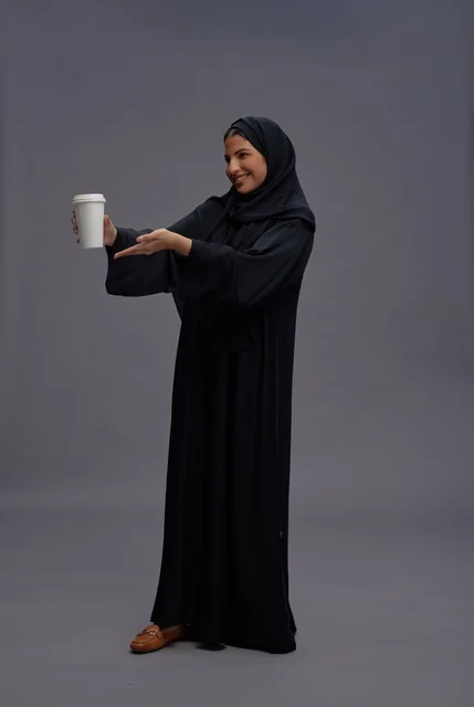 امرأة سعودية بعباءة سوداء تحمل كوب قهوة