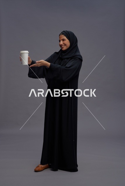 امرأة سعودية بالعباءة السوداء تحمل كوب قهوة في الاستوديو