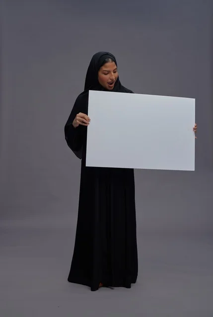 امرأة سعودية بعباءة سوداء تحمل لوحة بيضاء فارغة