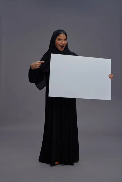 امرأة سعودية بالعباية تحمل لوحة بيضاء فارغة في استوديو