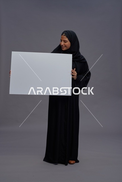 امرأة سعودية بعباءة سوداء تحمل لوحة بيضاء فارغة