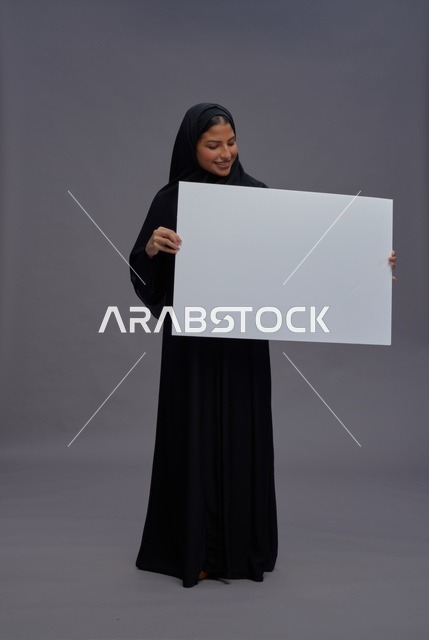 امرأة سعودية بالعباءة تحمل لوحة بيضاء فارغة