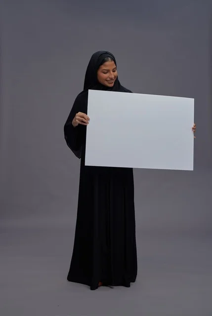 امرأة سعودية بالعباءة تحمل لوحة بيضاء فارغة