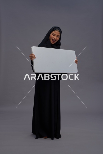 امرأة سعودية بعباية تحمل لوحة بيضاء فارغة للإعلان