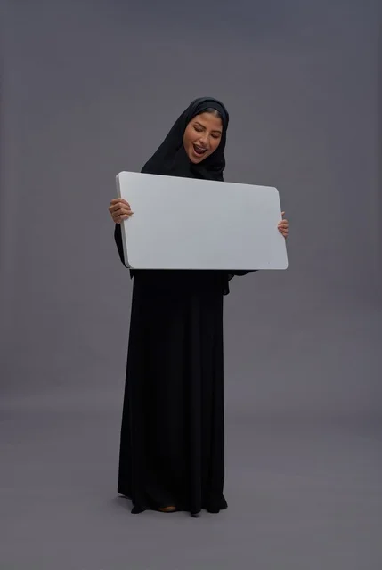 امرأة سعودية بعباية تحمل لوحة بيضاء فارغة للإعلان