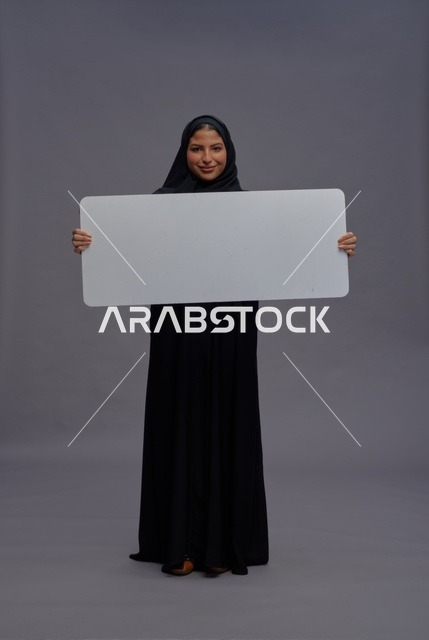 امرأة سعودية بعباءة سوداء تحمل لوحة بيضاء فارغة