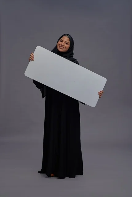 امرأة سعودية بعباية سوداء تحمل لوحة إعلانية بيضاء فارغة