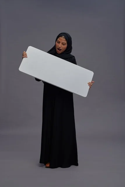 امرأة سعودية بعباية سوداء تحمل لوحة بيضاء فارغة